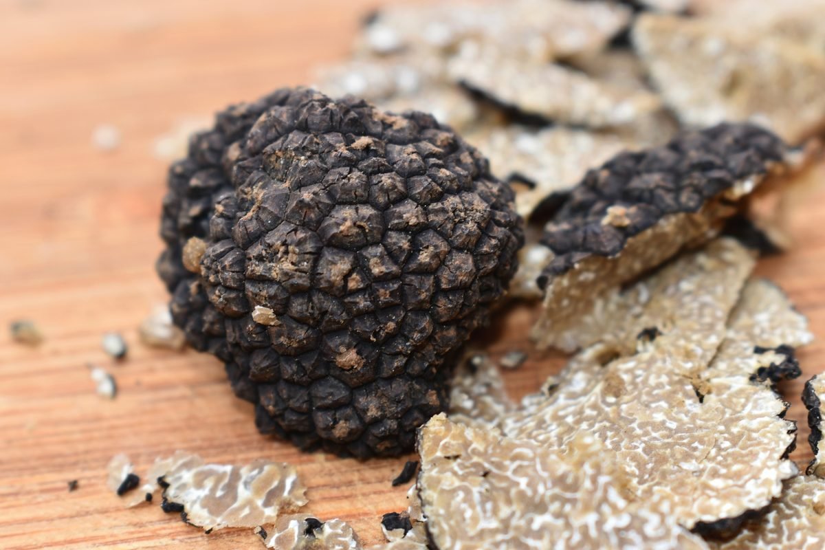 Un tartufo nero uncinato intero su un tagliere, circondato da fette sottili